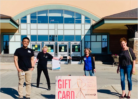 Des employés de Safeway remettent des cartes-cadeaux aux clients en respectant la distanciation physique.
